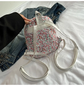 Detailansicht eines Blumen-Canvas-Rucksacks mit weißen Lederriemen auf weichem Bett