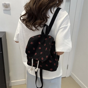Black corduroy backpack with strawberry print shown from a back perspective on a model