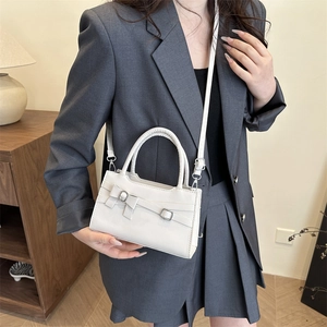 Elegant white crossbody bag with bow detail and top handle for women in indoor setting