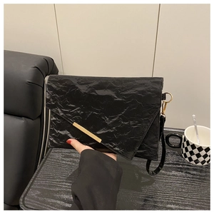Detail of black pleated clutch with gold metal trim and wrist strap accessory