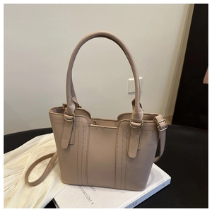 Detail of beige tote bag with round handles, vertical stitching and gold-tone metal hardware