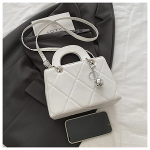 Close-up of white quilted PU handbag with large diamond patterns and silver ball charm