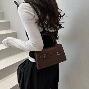 Dark brown leather handbag with bow detail and silver buckles on minimalist indoor stairs