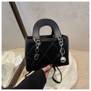 Close-up of black quilted leather handbag with silver ball charm and curved top handle