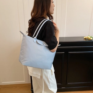 Grand sac cabas en nylon bleu clair avec rabat en cuir porté par un mannequin pour voyage