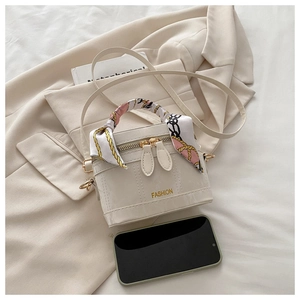 Close-up of beige box bag with silk scarf handle and gold lettering on blazer background
