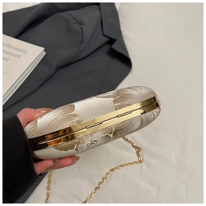 Close-up of white jacquard evening clutch bag with golden floral texture and chain