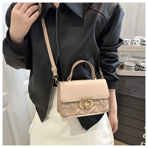 Detail of beige quilted crossbody bag with golden metal lock worn by a model