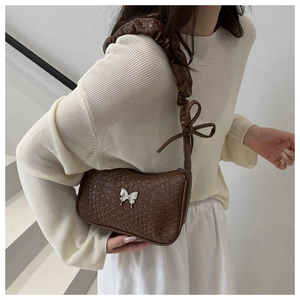 Detail of a brown woven shoulder bag featuring a silver butterfly and pleated bow strap