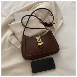 Détail du sac demi-lune en cuir marron avec boucle dorée à côté d'un smartphone