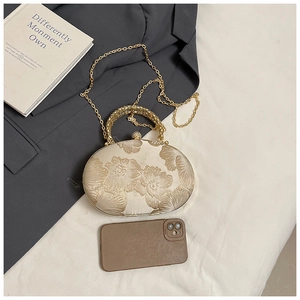 Macro detail of champagne gold evening bag with 3D floral embroidery and metal handles