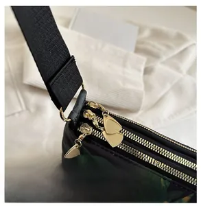 Detail of three-layer golden zippers and green leaf prints on black crossbody tote bag