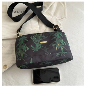 Detail of nylon tote bag featuring green leaf prints and gold-tone metal logo plaque