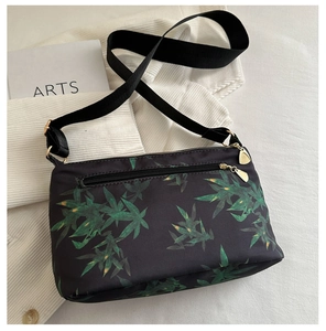 Detail of floral tote bag with green leaf prints, black nylon fabric, and golden zipper