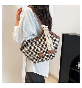 Detail of houndstooth tote bag featuring brown leather trim and wide canvas shoulder strap