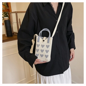 Detail of knitted cream crossbody phone bag with grey heart patterns and magnetic closure