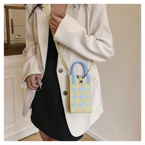 Mini yellow knitted crossbody phone bag with blue hearts shown on a model outfit