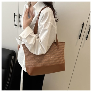 Detail of a woven straw tote bag with brown leather handles worn by a model