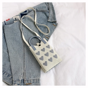 Détail d'un mini sac en tricot à motif cœur avec anse grise et bandoulière en cuir