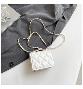 Detail of white quilted mini bag with gold-tone metal chain strap on textured fabric