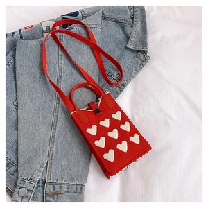 Détail du mini sac tricoté rouge avec motifs de cœurs blancs et fermeture à bouton noir
