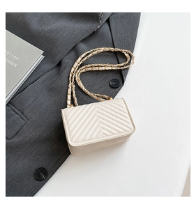 Detailed shot of cream quilted crossbody bag with gold chain strap on dark blazer