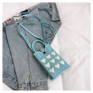 Détail du sac de téléphone en tricot bleu clair avec motif cœur blanc et poignée