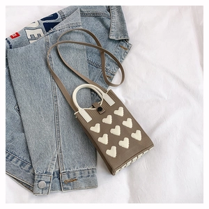 Close-up of brown knitted phone bag with white heart patterns and round top handles