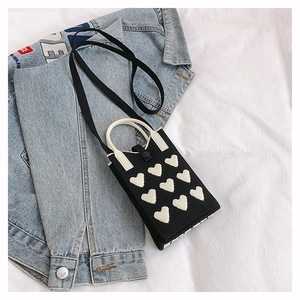 Détail du mini sac en tricot à motif cœur sur veste en jean montrant texture et sangles