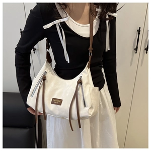 Detail of white half-moon shoulder bag with brown tassels and a leather brand plate