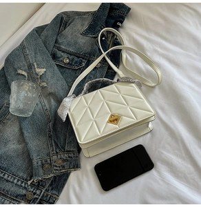 Detailed view of white quilted crossbody bag with gold twist lock and paisley scarf handle
