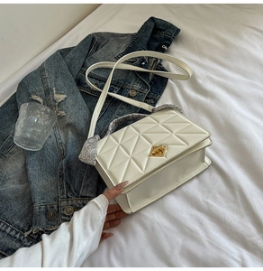 Close-up of white quilted crossbody bag with silk scarf handle and golden twist lock