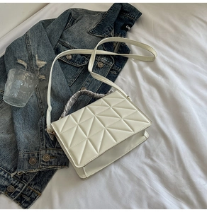 Detailed view of white quilted crossbody bag with vintage silver floral handle on blue denim