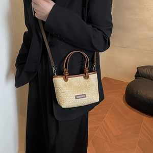 Straw crossbody bag with brown leather trim shown on a model in a minimalist room