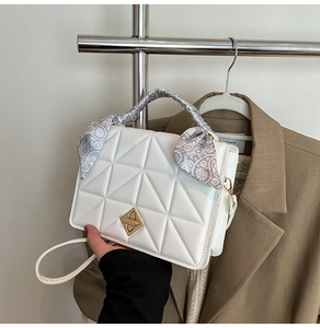 Detail of white quilted handbag featuring gold diamond clasp and silk scarf wrapped handle