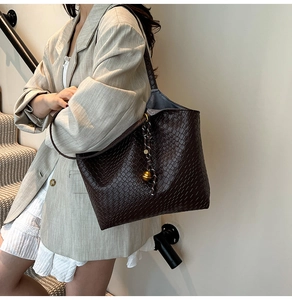 Detail of dark brown woven tote bag with metallic ball charm and braided rope knot