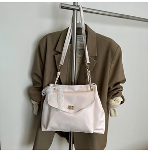 Détail du sac crème avec fermoir rotatif doré et décoration de nœud en dentelle blanche
