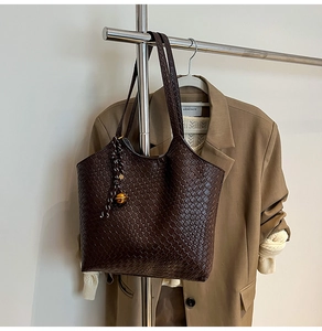 Detail of deep brown woven leather tote bag with golden spherical pendant and charm