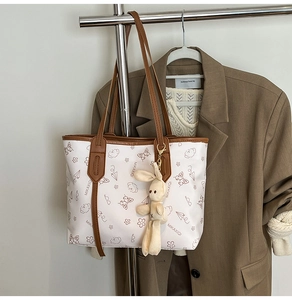 Détail du sac cabas blanc avec illustrations, anses brunes et breloque lapin en tricot