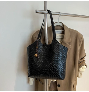 Detail of black woven tote bag with gold metal ball tassel on khaki blazer