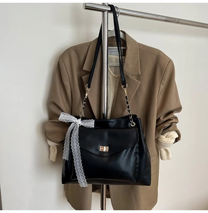 Détail du sac à bandoulière en cuir mat noir avec fermoir doré et nœud en dentelle blanche