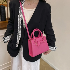 Mini sac carré rose avec nœud et détails dorés porté par un mannequin en tailleur