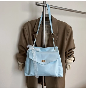 Détail du sac bandoulière bleu clair avec boucle dorée et nœud décoratif en dentelle blanche
