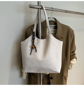 Detail of white woven leather tote bag featuring woven texture and hanging bell charm
