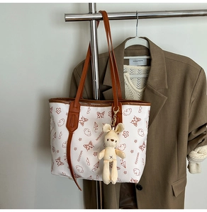 Détail du sac cabas blanc avec motif d'ours et breloque lapin sur un cintre en métal