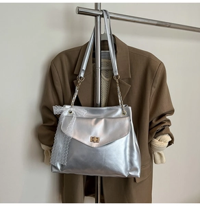 Détail du sac à main argenté avec fermoir doré rotatif et nœud décoratif en dentelle blanche