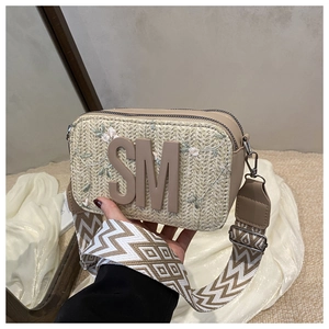 Dettaglio borsa fotografica beige intrecciata con ricamo floreale, logo SM e tracolla larga