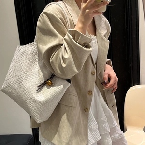 White woven tote bag with gold bell charm shown in a minimalist mirror selfie style
