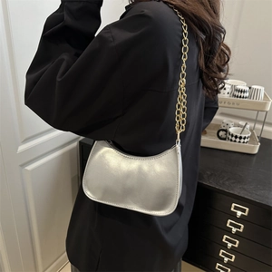 Silver crescent hobo bag with thick gold chain strap shown in a modern home setting