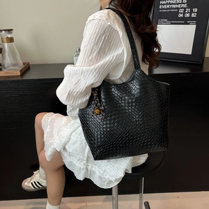 Minimalist black woven tote bag with brass bell pendant shown on model's shoulder